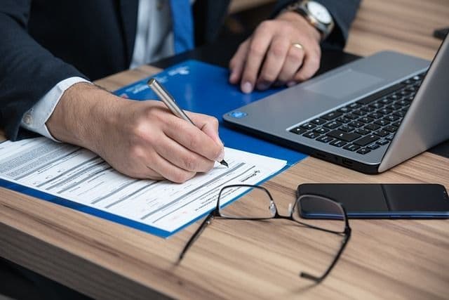 Professionnel signant un document à un bureau équipé d'un ordinateur